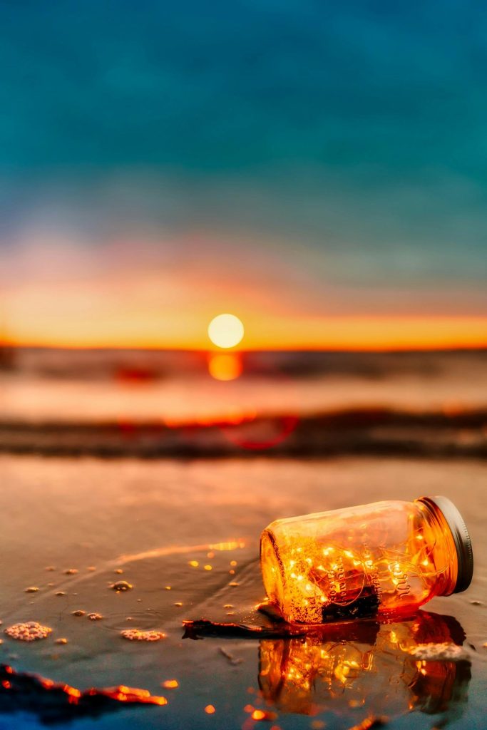 pexels-photo-462030-462030 A lit jar with lights sits on a beach, creating a tranquil scene during sunset.