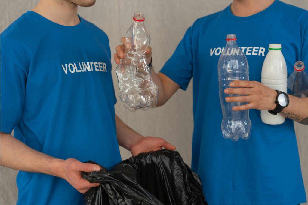 pexels-photo-7475428-7475428 Two volunteers in blue shirts collect plastic bottles for recycling, showcasing community involvement.